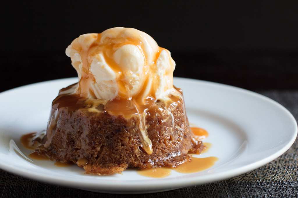 Sticky toffee pudding cake on a plate with vanilla ice cream and caramel sauce on top