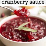 cranberry sauce in a white dish with fresh sage on top and a spoon holding a bite of sauce