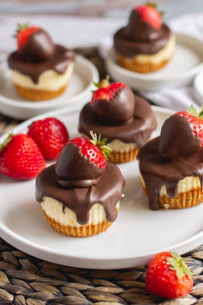 mini cheesecakes on a plate with chocolate covered strawberries on top and chocolate dripping down