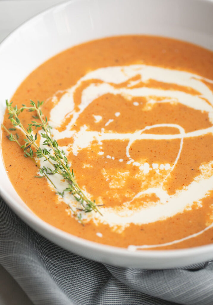 roasted red pepper and tomato soup with a swirl of cream and garnished with fresh thyme