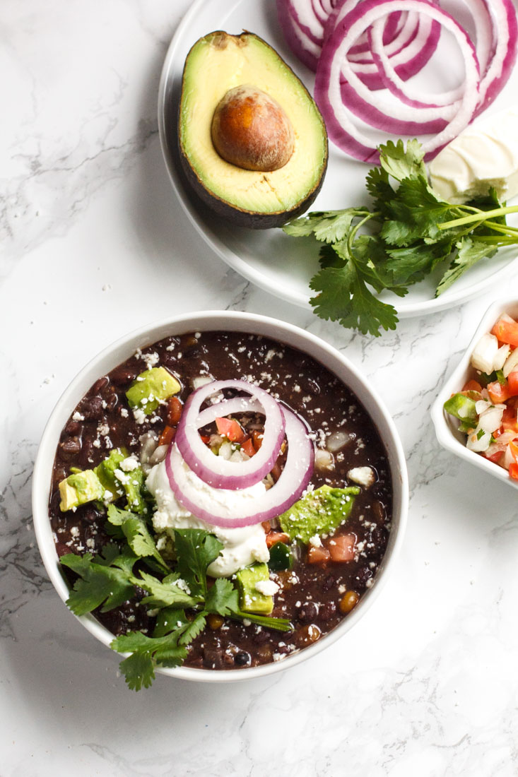 slow cooker black bean soup in a bowl with cilantro, avocado and sour cream