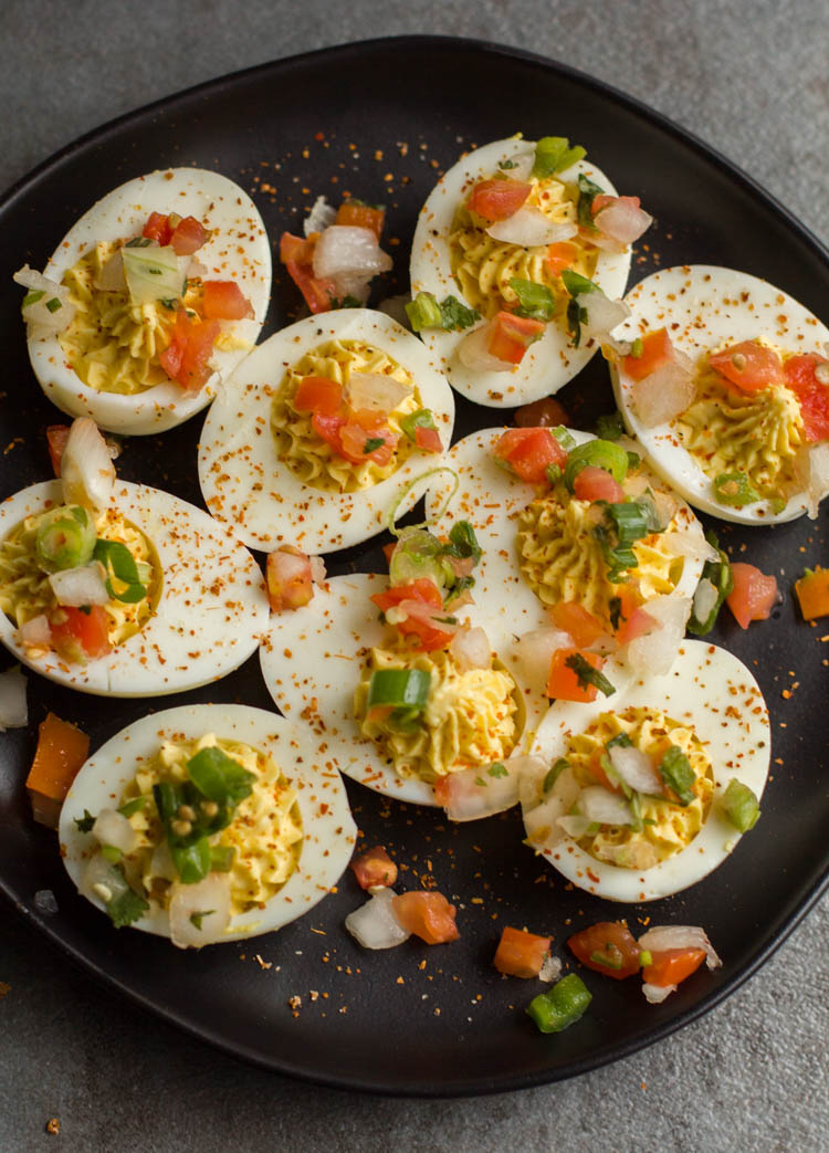 deviled eggs on a black plate topped with pico de gallo