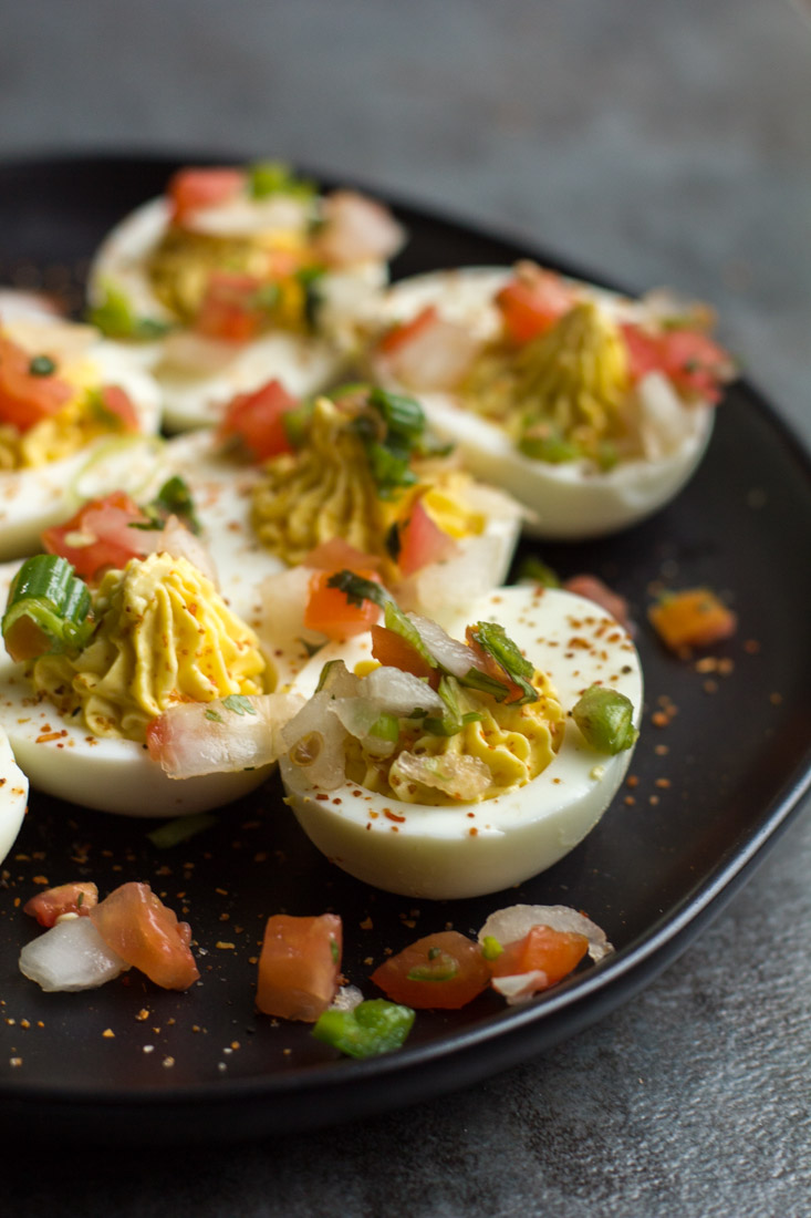 hard boiled deviled eggs on a black plate with tomato and onion on top