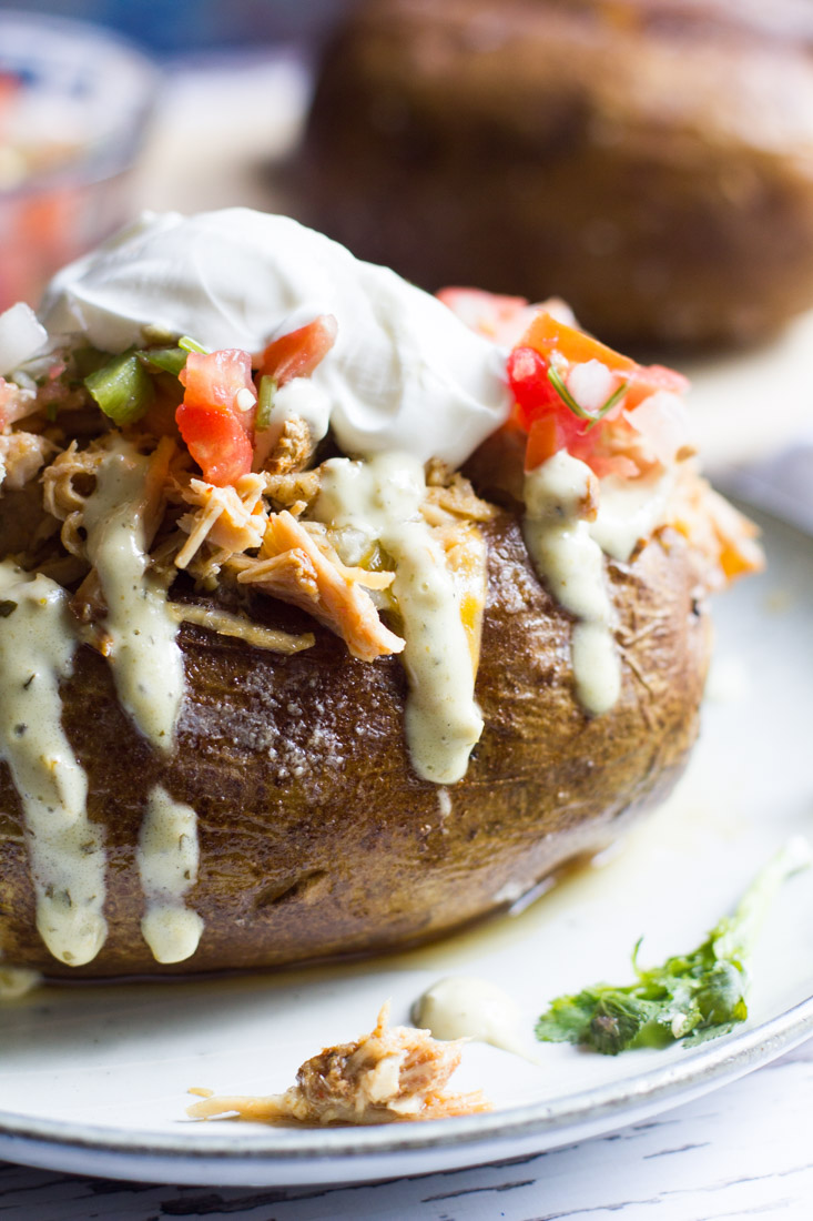 These easy Tex Mex loaded baked potatoes are topped with a slow cooked Tex Mex style pulled pork, cheese, pico de gallo and jalapeno ranch. A hearty and easy to prepare meal!