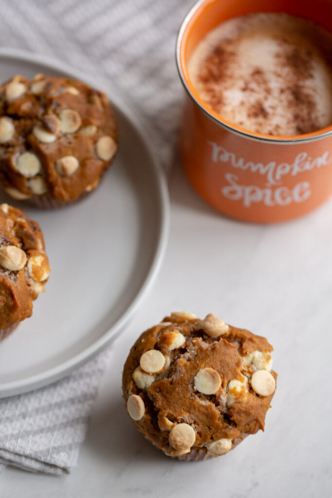 bakery style white chocolate chips pumpkin muffins on a white plate with a coffee