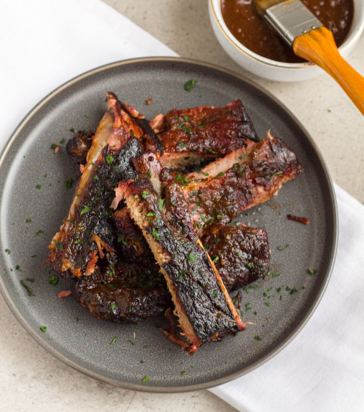 smoked ribs on a plate with sauce on the side