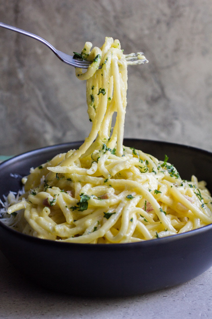 creamy pancetta carbonara in a bowl with a fork pulling noodles away to eat