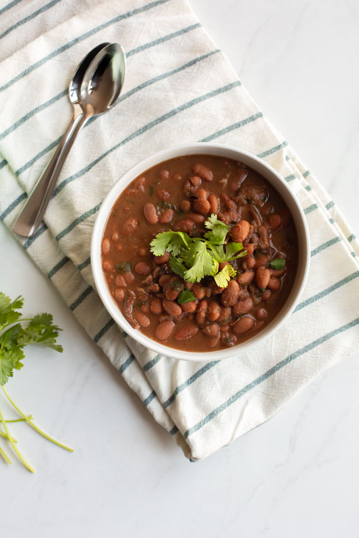 Instant Pot Charro Beans in a white bowl on a white cloth with cilantro on top