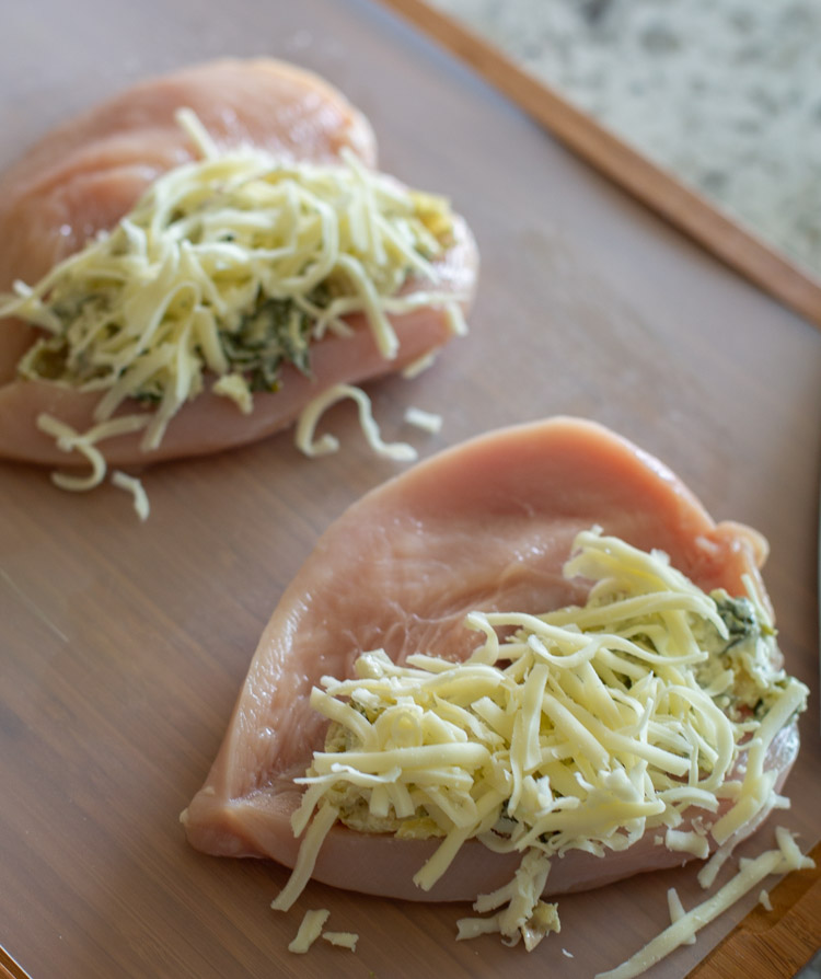 raw chicken being stuffed with spinach artichoke dip