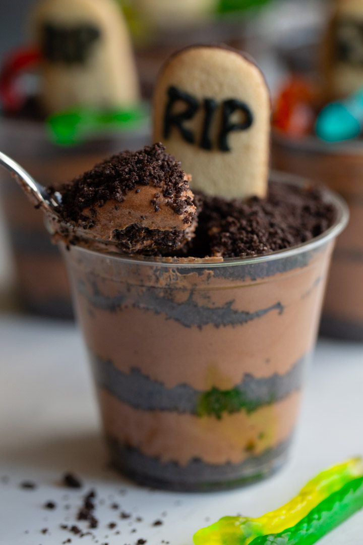 baileys chocolate mousse cups with layers of oreo dirt, gummy worms and a cookie tombstone with a bite taken out