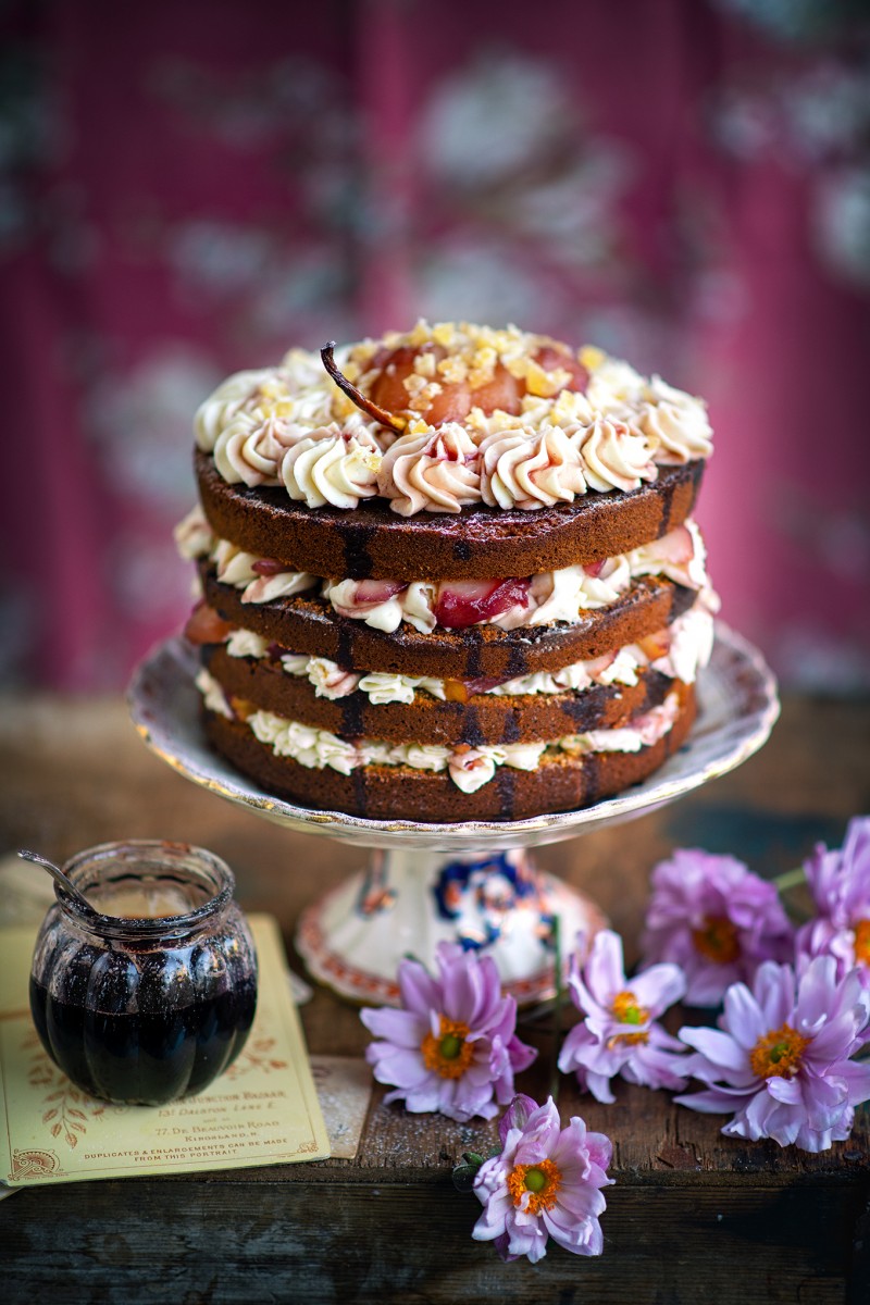 ginger pear cake on a stand and purple flowers below against a pink and blue background