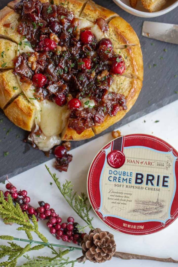 baked brie with cranberries and bacon with joan of arc brie on the table