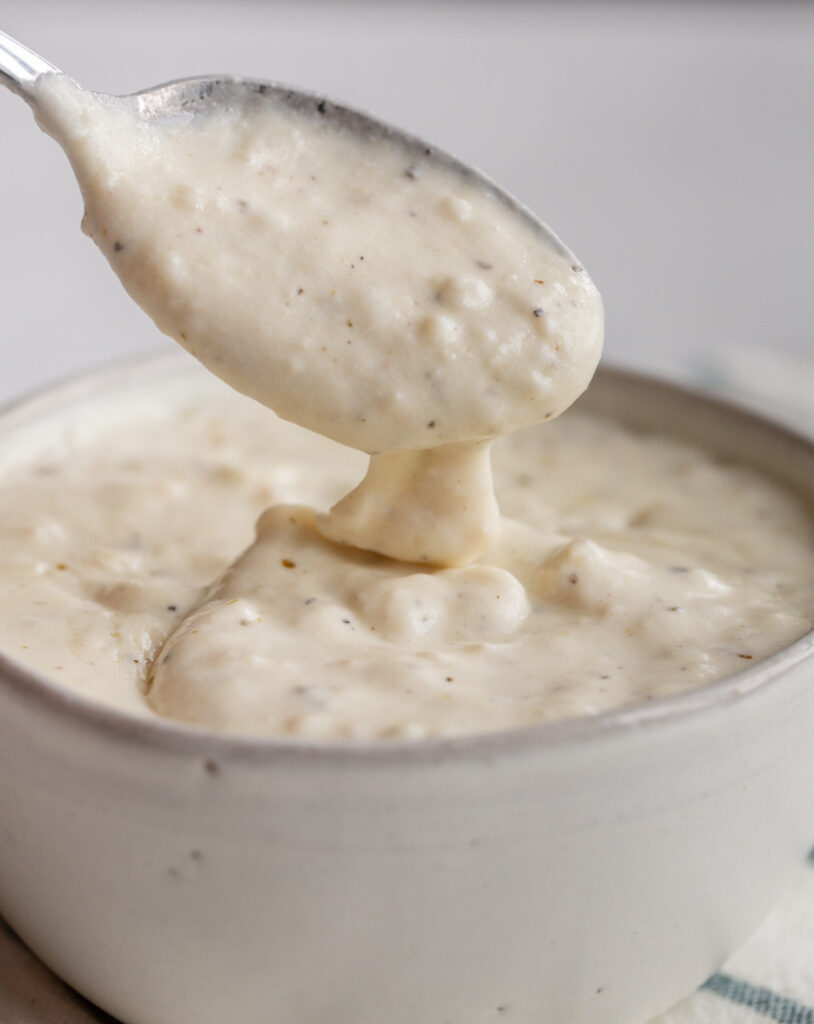 Garlic pizza sauce in a bowl with a spoon dripping
