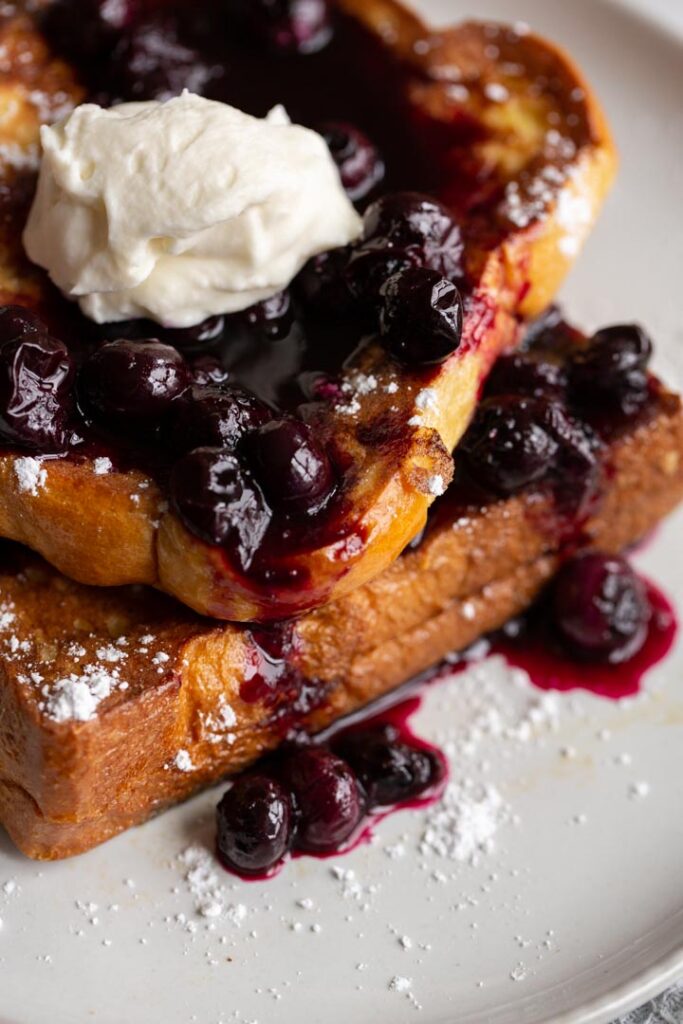a closeup of blueberry stuffed french toast with blueberry sauce and cream on top