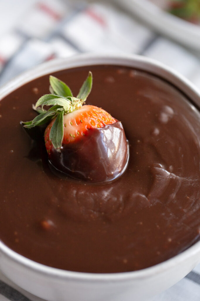 a strawberry in a bowl of hot fudge sauce