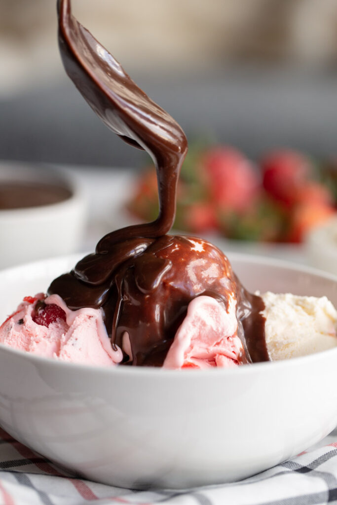 hot fudge sauce being poured on a bowl of ice cream