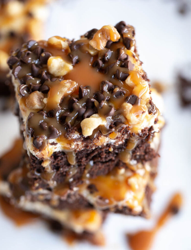 turtle cheesecake brownies stacked high with caramel sauce dripping