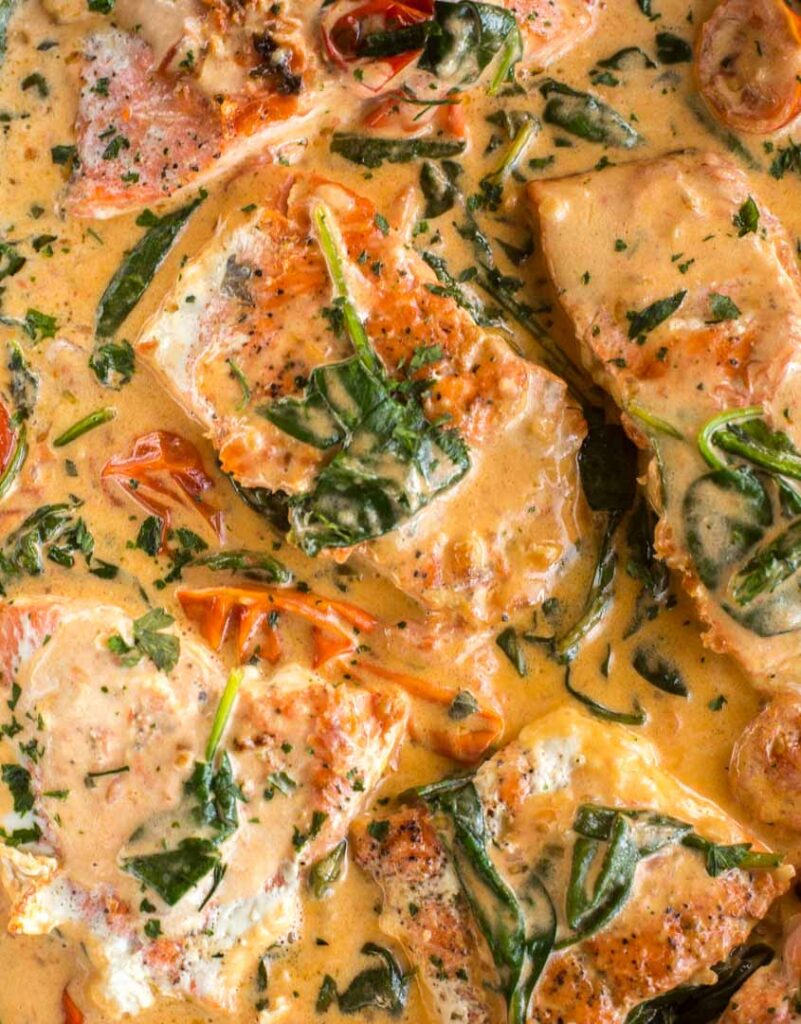 pan seared salmon served in a creamy sauce with spinach and tomatoes
