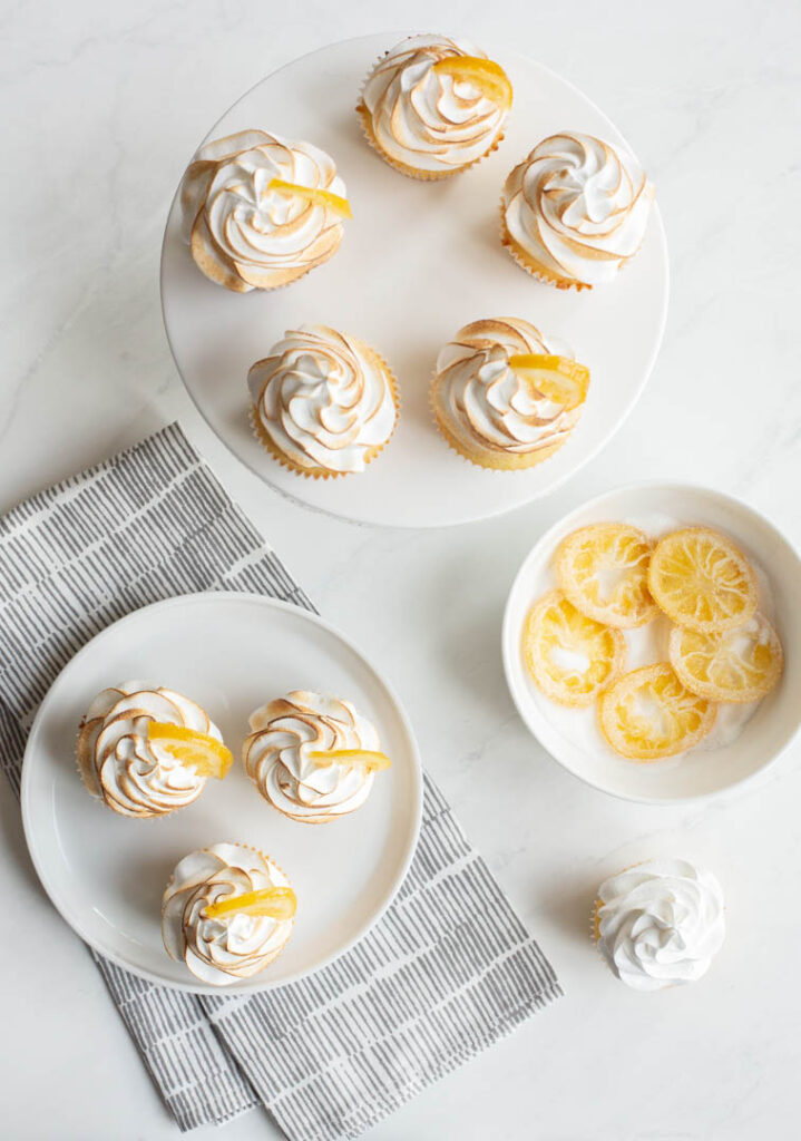 lemon meringue cupcakes on a plate on a table with candied lemons on the side