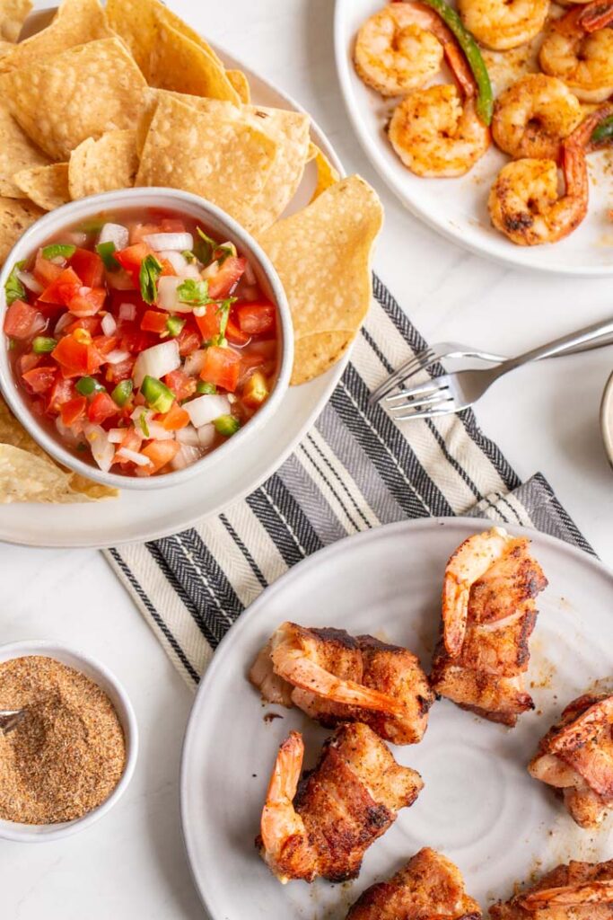 stuffed shrimp en brochette on a plate with chips and salsa in the back
