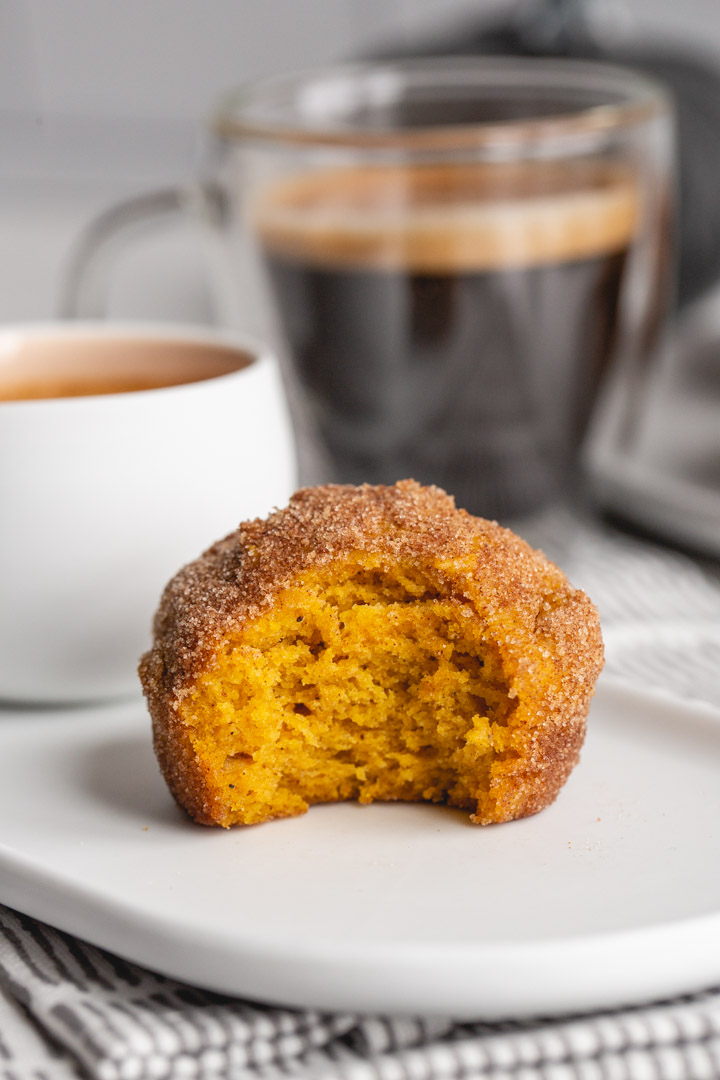a pumpkin muffin rolled in cinnamon sugar on a plate with a cup of coffee