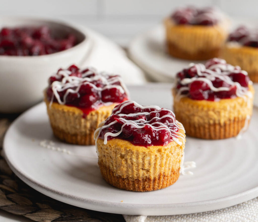 mini pumpkin cheesecakes on a plate topped with cranberry compote and white chocolate