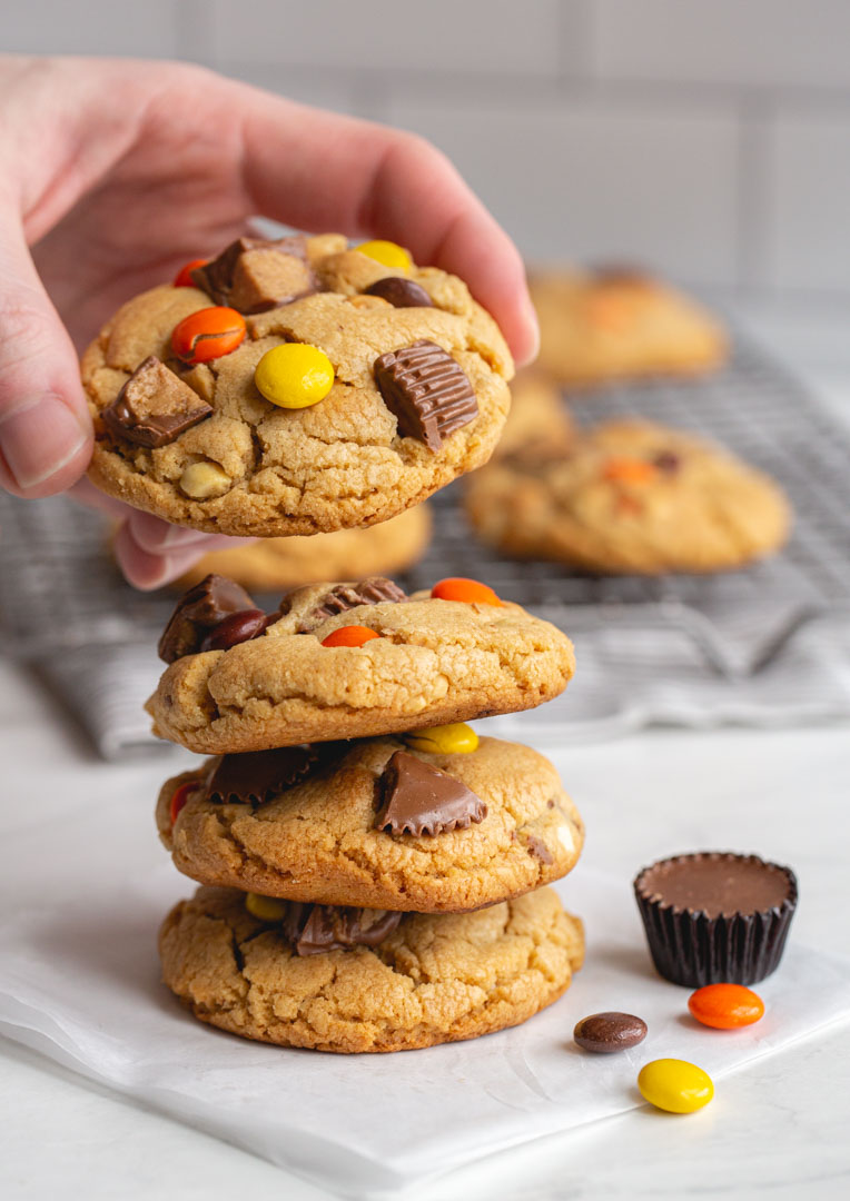 hand placing peanut butter cup cookie on top of large stack of cookies
