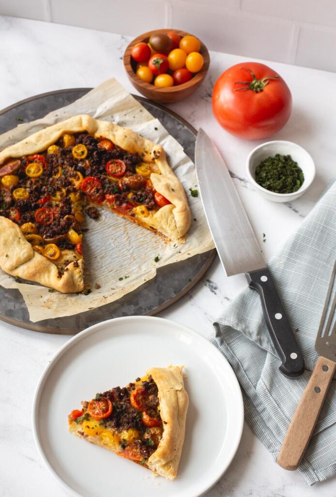 tomato galette with impossible meat and fresh basil on a serving dish with a slice removed