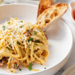 creamy lobster linguine in a bowl with two slices of sourdough bread