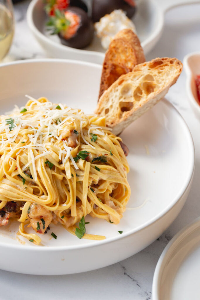 creamy lobster linguine in a bowl with two slices of sourdough bread