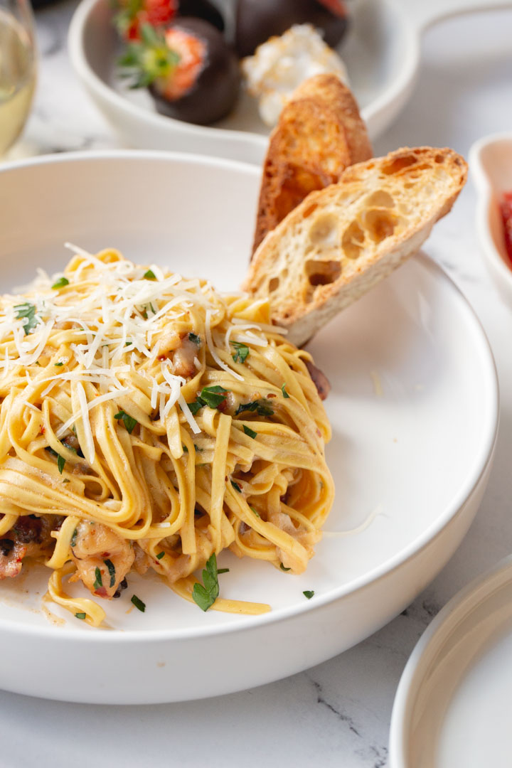 creamy lobster linguine in a bowl with two slices of sourdough bread