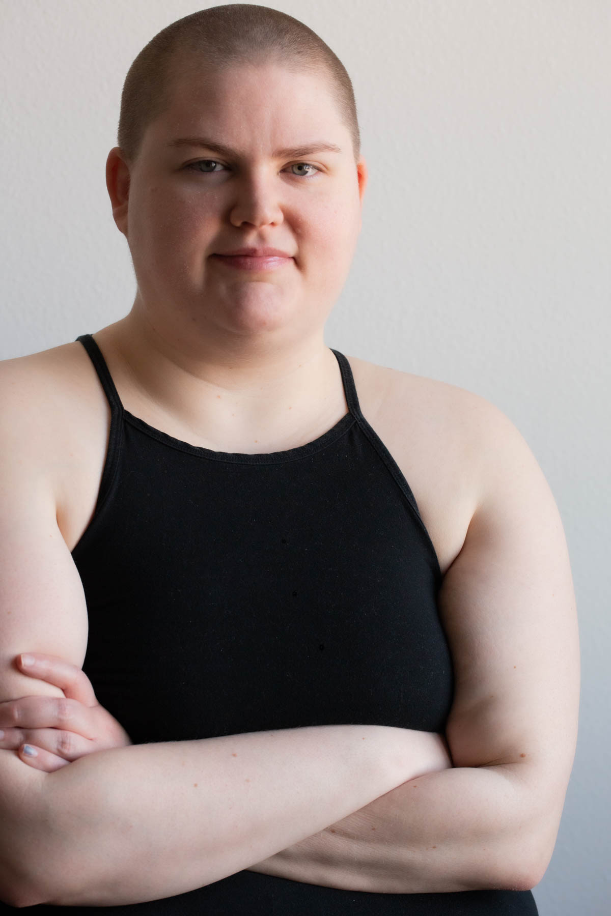 a person with a shaved head wearing a black shirt crossing their arms and looking into the camera