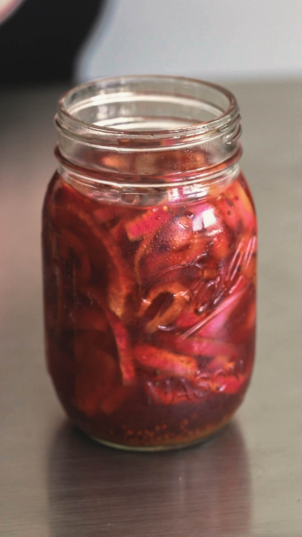 red onions and brine in a mason jar on a stainless steel counter