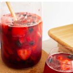 rosé sangria in a pitcher with a large wooden spoon, text on top reads: rosé sangria with mixed summer berries