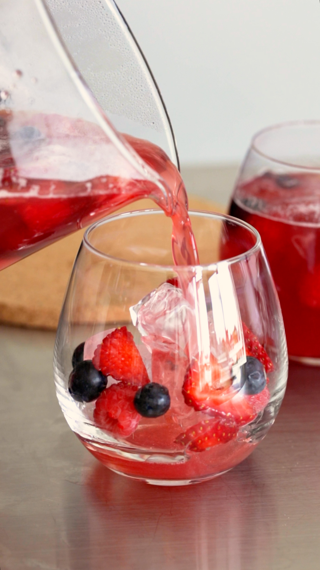 a stemless wine glass with ice, strawberries, blueberries and raspberries with rose sangria being poured into it from a large pitcher