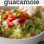 white bowl with guacamole and pico de gallo with a tortilla chip sticking out and a sliced lemon in the background