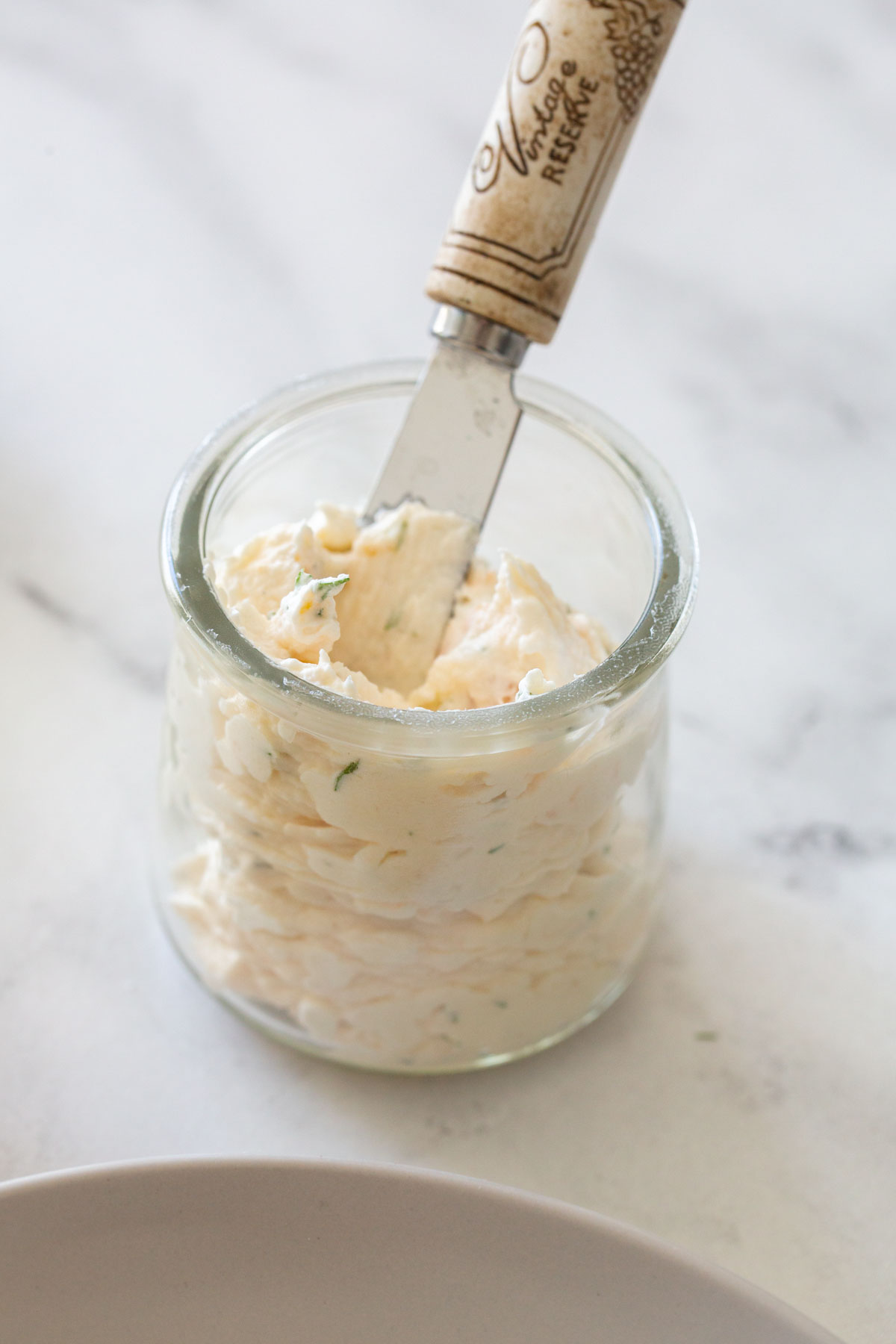 smoked salmon mousse in a clear jar with a spreader against a white marble backdrop